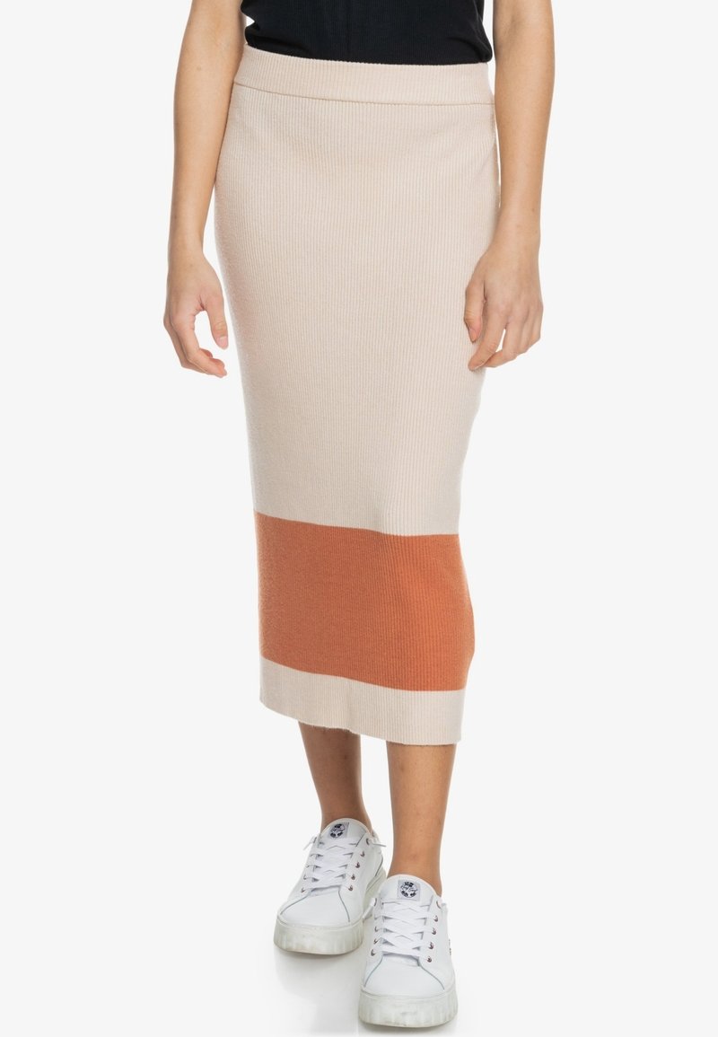 Jupe mi-longue côtelée beige avec une bande horizontale orange et blanche. Texture douce, coupe ajustée, portée avec des baskets blanches.