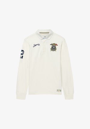 Polo blanco de manga larga con texto bordado "Superdry" en el pecho, parche azul marino con número en la manga derecha y escudo multicolor en el pecho izquierdo.