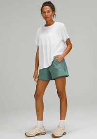 Witte t-shirt met korte mouwen en een ronde hals, gecombineerd met groene sportshorts met zijzakken. Crème sneakers maken de outfit compleet.