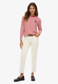 Rood-witte gestreepte longsleeve shirt met een ronde halslijn en geborduurde details, gecombineerd met een witte broek en donkere instappers.