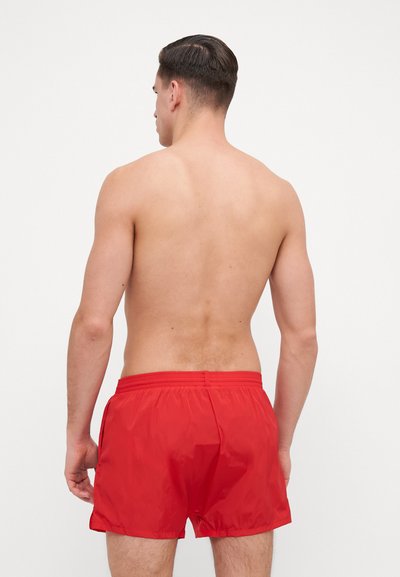 Shorts de înot roșii cu un brâu elastic, buzunare laterale și o textură netedă, văzute din spate.