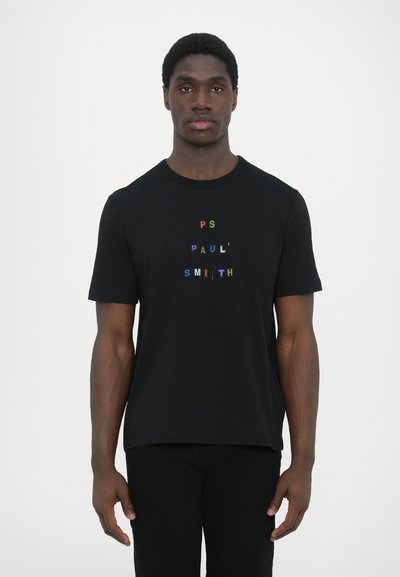 T-shirt noir en coton avec des manches courtes, affichant un texte multicolore 'PS PAUL SMITH' en design central. Texture lisse, style col rond.