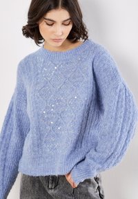 Hellblauer Pullover aus flauschigem Material, mit einem strukturierten Rautenmuster, verziert mit Pailletten und gerippten Bündchen.