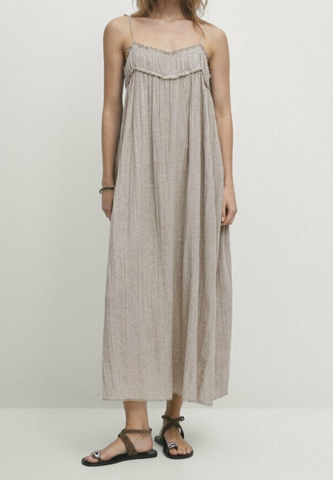 Robe maxi marron clair avec des bretelles fines, un buste froncé et un tissu plissé fluide. Associée à des sandales noires plates et une bride cheville marron.