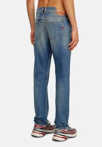 Jeans de mezclilla azul con un corte recto, que cuentan con una etiqueta en la parte trasera, dos bolsillos traseros y un sutil desgaste. Llevados con zapatillas.