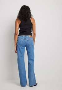 Augstos vidukļa zilo džinsus ar taisnu kāju griezumu, ar aizmugurējām kabatām un brūnu zīmola birku jostasvietā.