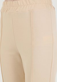 Beige stretch pants with an elastic waistband, smooth texture, and side seams. Minimalist design, no visible hardware or patterns.