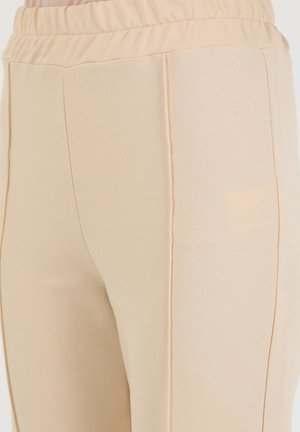 Beige stretch pants with an elastic waistband, smooth texture, and side seams. Minimalist design, no visible hardware or patterns.