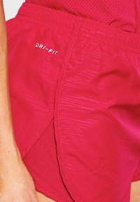 Primer plano de pantalones cortos deportivos Dri-FIT rojos con tela texturizada y panel lateral de malla, llevados por una persona.