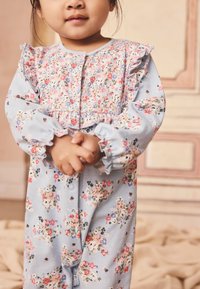 Floral-patterned blue jumpsuit with ruffled sleeves and button down front. Features small flowers in pink, purple, and yellow on soft fabric.