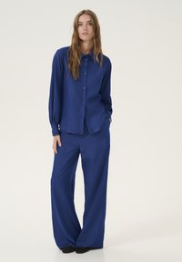Camicia blu a maniche lunghe con bottoni e pantaloni larghi abbinati, realizzati in un tessuto morbido, caratterizzati da una vestibilità comoda e una texture sottile.