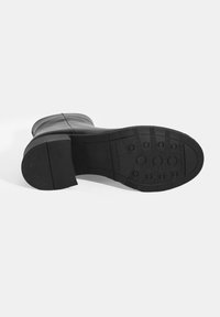 Semelle de botte en cuir noir avec une surface texturée, un talon rectangulaire et des motifs de prise circulaires. Matériau en caoutchouc durable pour l'adhérence.