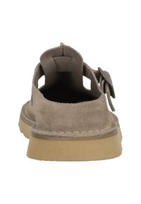 Beige suede shoe with open design, back strap, and stitched accents. Rubber sole with a textured finish and slight elevation.