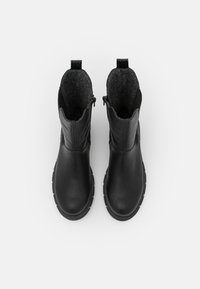 Bottes de cheville en cuir noir avec un intérieur texturé gris, des fermetures éclairs sur les côtés et une semelle robuste. Équipées de languettes en boucle pour un enfilage facile.