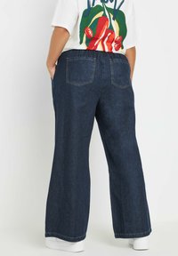 Laahustavat tummat farkut, joissa on kaksi takataskua, istuva vyötärö ja rento ulkonäkö, yhdistettynä valkoiseen graafiseen t-paitaan.