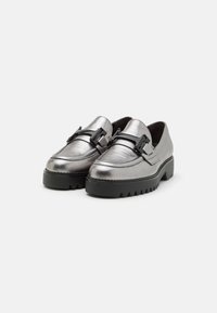 Metallisch zilveren loafers met een stevige zwarte zool, voorzien van een decoratieve zwarte gesp en stikdetails langs de randen.