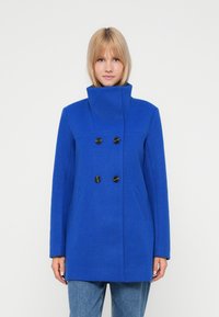 Cappotto di lana blu con colletto alto, design doppiopetto, bottoni neri e tasche laterali. Presenta una vestibilità dritta e una texture liscia.