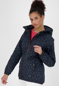 Giacca blu navy con cappuccio, caratterizzata da un motivo a pois in azzurro chiaro. Zip e dettagli marroni, polsini elastici e vita aderente.