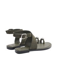 Zielone zamszowe sandały z regulowanymi paskami wokół kostki, metalicznymi akcentami, otwartym noskiem i płaską podeszwą. Charakterystyczny detal z zapięciem klamrowym.