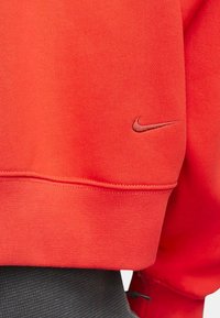 Sudadera roja con cuello redondo y dobladillo de canalé, con un logotipo de Nike sutilmente bordado en un tono de rojo más oscuro.