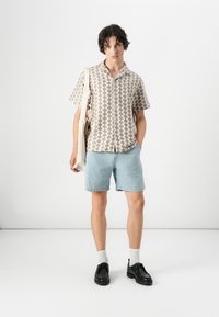 Short-sleeve shirt with a tan and cream zigzag pattern, paired with light blue denim shorts and black shoes, carrying a beige tote bag.