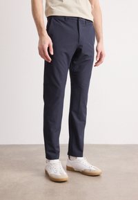 Marina blå byxor av lättviktsmaterial med rak bendesign, med platt fram, bältesöglor och fickdetaljer, kombinerat med vita sneakers.