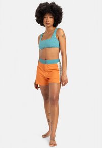 Svetlomodrý textúrovaný crop top v kombinácii s oranžovými šortkami. Šortky majú kontrastný modrý pás a bočný panel v svetlom odtieni.