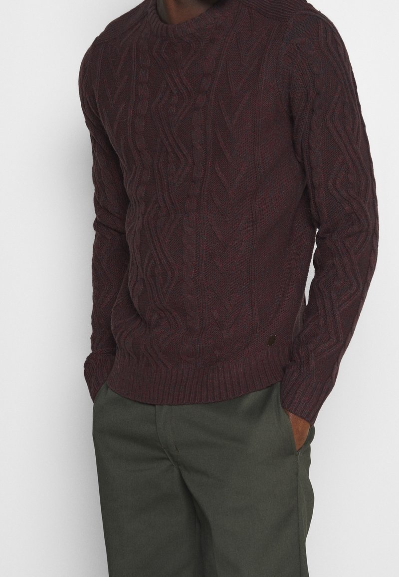 Dunkelburgunderfarbener Strickpullover aus Wolle, mit Rundhalsausschnitt, gerippten Bündchen und Saum, sowie strukturierten Mustern und einem kleinen Logo-Detail.