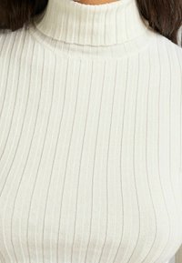 Vit räfflad polotröja med en strukturerad textile, med hög hals och vertikala ränder över hela ytan.