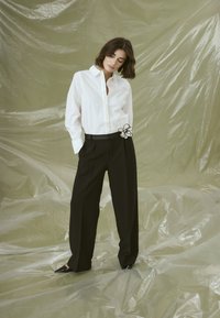 White button-up shirt with embellished front, paired with black wide-leg trousers featuring a fabric flower accent on the waistband.