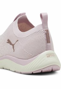 Sneaker en maille rose clair avec une surface texturée, semelle confortable, et un accent logo marron. Présente un design à enfiler et une languette.