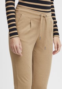 Beige joggers med en texturerad yta, snörning med silverfärgad spets och sidofickor. Kombinerade med en långärmad topp i svart och tan-randig.