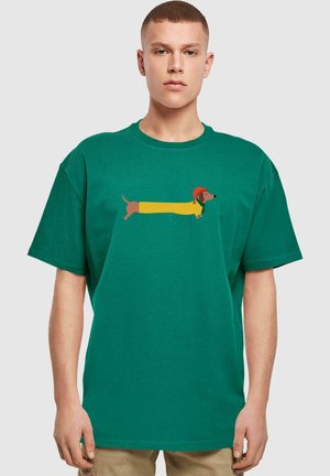 Grøn bomulds t-shirt med en illustration af en dachshund i gult med en rød hat, der fremhæver en afslappet, oversized pasform.