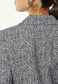 Blazer im Schäfchenmuster mit einem schwarz-weißen Farbschema, glatter Textur und einem klassischen Kragen mit sichtbaren Nähdetails.