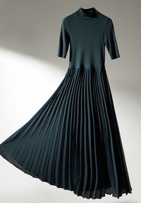 Mörkgrön klänning med korta ärmar och hög halsringning. Kjolen har vertikala veck som skapar en texturerad, flödande design.