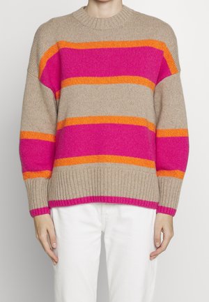 Pull en maille beige avec de larges rayures horizontales roses et des rayures étroites oranges, porté avec un pantalon blanc.
