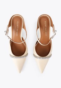 Kremowe skórzane szpilki na pasku typu slingback z zaostrzonymi czubkami i paskiem ozdobionym kryształkami. Posiadają brązową wkładkę i regulowaną sprzączkę.