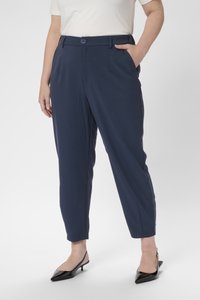 Pantalones navy hechos de una tela suave, con cierre de botón, bolsillos laterales y un diseño de pierna ajustada. Combinados con tacones negros.