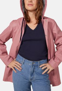 Wasserabweisende pinke Regenjacke mit gestreifter Kapuze, Druckknopfverschlüssen und taillierten Ärmeln, kombiniert mit einem marineblauen V-Ausschnitt-Shirt und hoch taillierten Jeans.