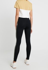 Svarta leggings med en tight passform, med sidostråk i neon-gult. Parat med en kortärmad t-shirt i beige och vitt. Mockaskor.