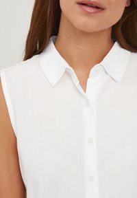 Vit ärmlös blus med klassisk krage, framknäppning och mjukt, lätt tyg.