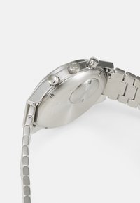 Silberner Edelstahl-Uhren mit eckigem Gehäuse, strukturiertem Krone und Gliederarmband. Die Rückseite ist glatt mit gravierten Details.