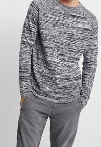 Pull à manches longues et col rond en maille chinée bleu marine et blanc. Il présente des manches raglan et un col texturé. Tissu doux.