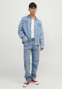 Jachetă din denim de culoare albastru deschis, purtată împreună cu un tricou alb și blugi albaștri deschisi. Adidași roșii completează ținuta. Se poartă o șapcă neagră.
