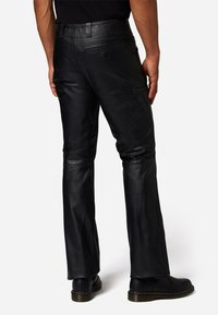 Zwarte leren broek met een gladde textuur, rechte snit en subtiele details op de achterzakken. Gepaard met zwarte schoenen.