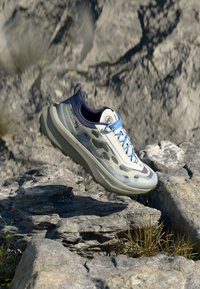 Leichte Laufschuhe in Hellgrau mit blauen Akzenten, ausgestattet mit einem strukturierten Mesh-Obermaterial, einer gepolsterten Sohle und einer multidirektionalen Griffsohle.