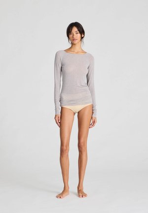 Svijetlosiva majica s dugim rukavima izrađena od mekog, laganog materijala. Dizajn sadrži okrugli izrez i uski kroj. Uparena je s bež donjim rubljem.