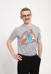 Grå bomulds t-shirt med et farverigt grafisk motiv af en pony og en regnbue, med teksten "Følg din egen regnbue." Sammen med sorte bukser.