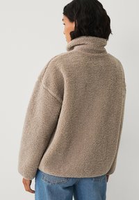 Veste en polaire grise avec un col montant, une coupe oversize et une texture apparente. Associée à un jean en denim bleu clair.