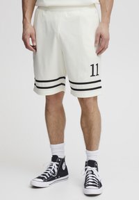 Hvide mesh basketballshorts med sorte striber ved kanten og nummer 11 på venstre ben. Båret med sorte hightop sneakers og hvide sokker.